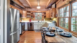 A rustic kitchen with wooden cabinets, a stainless steel refrigerator, and a dining table set for six. - Cozy 4-bedroom cabin with separate living spaces, and all the amenities. (Sevierville)