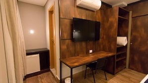 A compact room with a wooden desk, a chair, a television mounted on the wall, and a wardrobe with a towel hanging inside. - Adria Premium Hotel (Guarapuava)