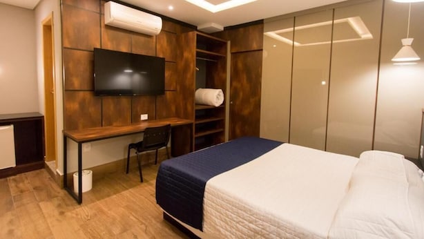 A modern bedroom with a bed, a desk, a chair, a TV, and a wardrobe. - Adria Premium Hotel (Guarapuava)