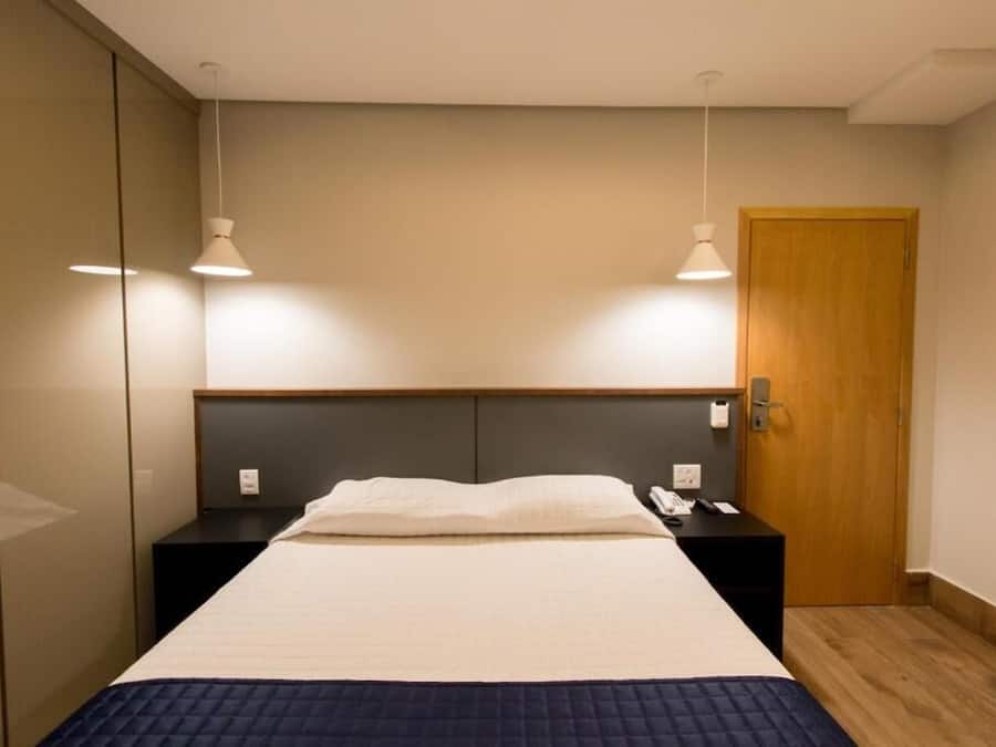 Una habitación de hotel moderna con una cama, mesitas de noche, una puerta de madera e iluminación colgante.
