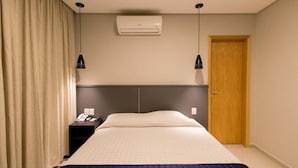A hotel room with a bed, an air conditioning unit, a nightstand, a telephone, and a door. - Adria Premium Hotel (Guarapuava)