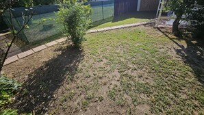 A backyard with a small tree, a fenced area, and a building in the background. - Monolocale Elena - Quartu Sant'e... (Quartu sant'elena)