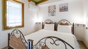 A bedroom with a bed, wooden headboard, bedside tables, and wall-mounted air conditioning unit. - Monolocale Elena - Quartu Sant'e... (Quartu sant'elena)