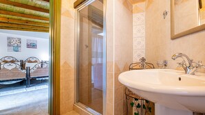A bathroom with a shower, sink, and a bed with a metal frame. - Monolocale Elena - Quartu Sant'e... (Quartu sant'elena)