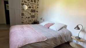 A bedroom with a bed, a bedside lamp, a round mirror, and a stone wall. - 4* gîte 15 minutes from Puy du Fou with heated swimming pool (Mortagne-sur-Sèvre)