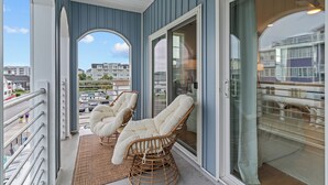 Un balcon avec des fauteuils en osier, une vue sur la ville et une porte vitrée donnant sur un espace extérieur.