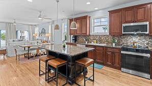 Une cuisine moderne dotée d’un grand îlot central, de meubles en bois, d’appareils électroménagers en acier inoxydable et d’un coin repas avec un canapé et des chaises.