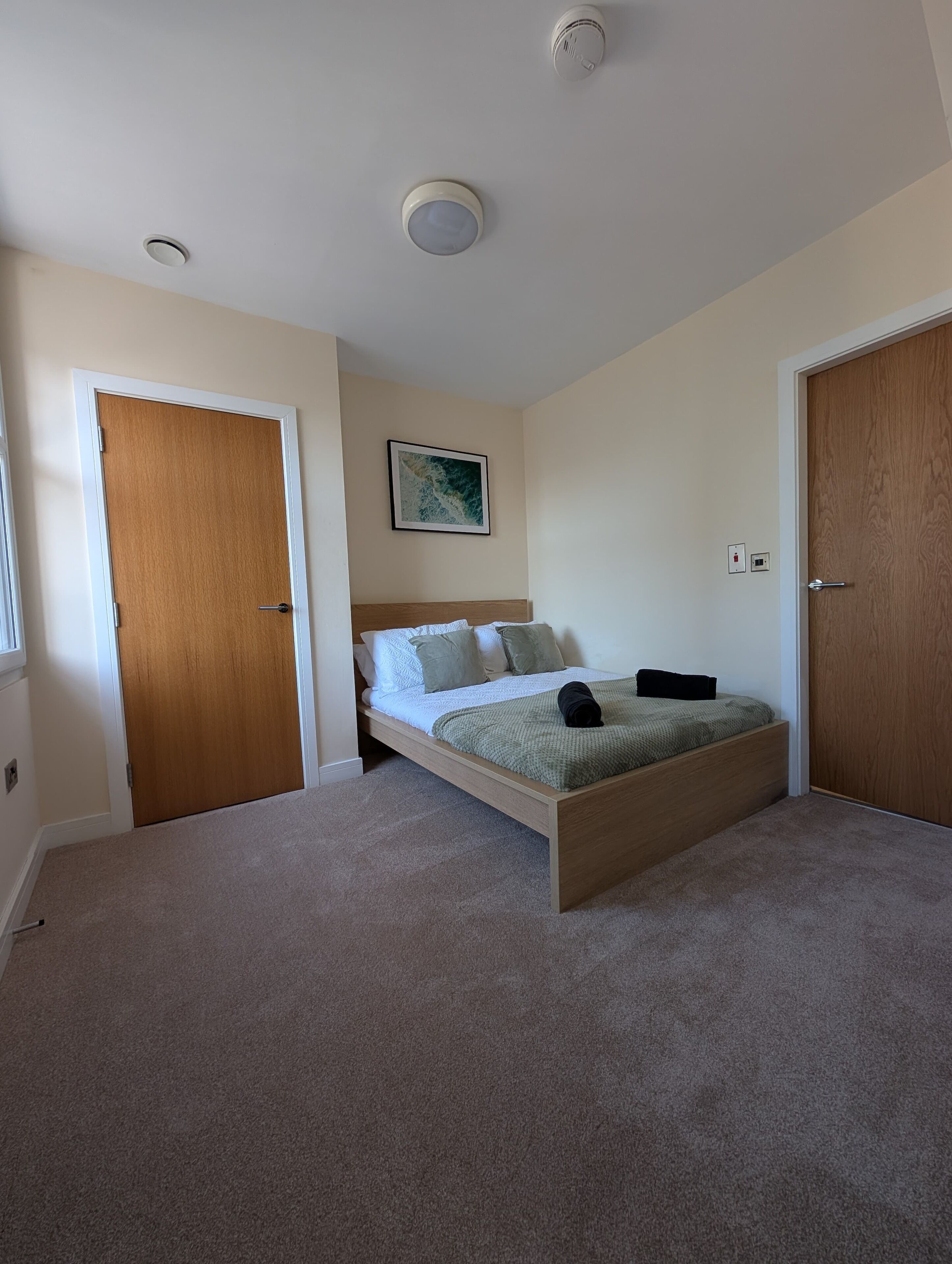 A bedroom with a wooden bed frame, a headboard, a green blanket, and a pillow. There is a wooden door on the left and a wooden closet on the right.