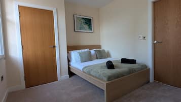A bedroom with a wooden bed frame, a headboard, a green blanket, and a pillow. There is a wooden door on the left and a wooden closet on the right.