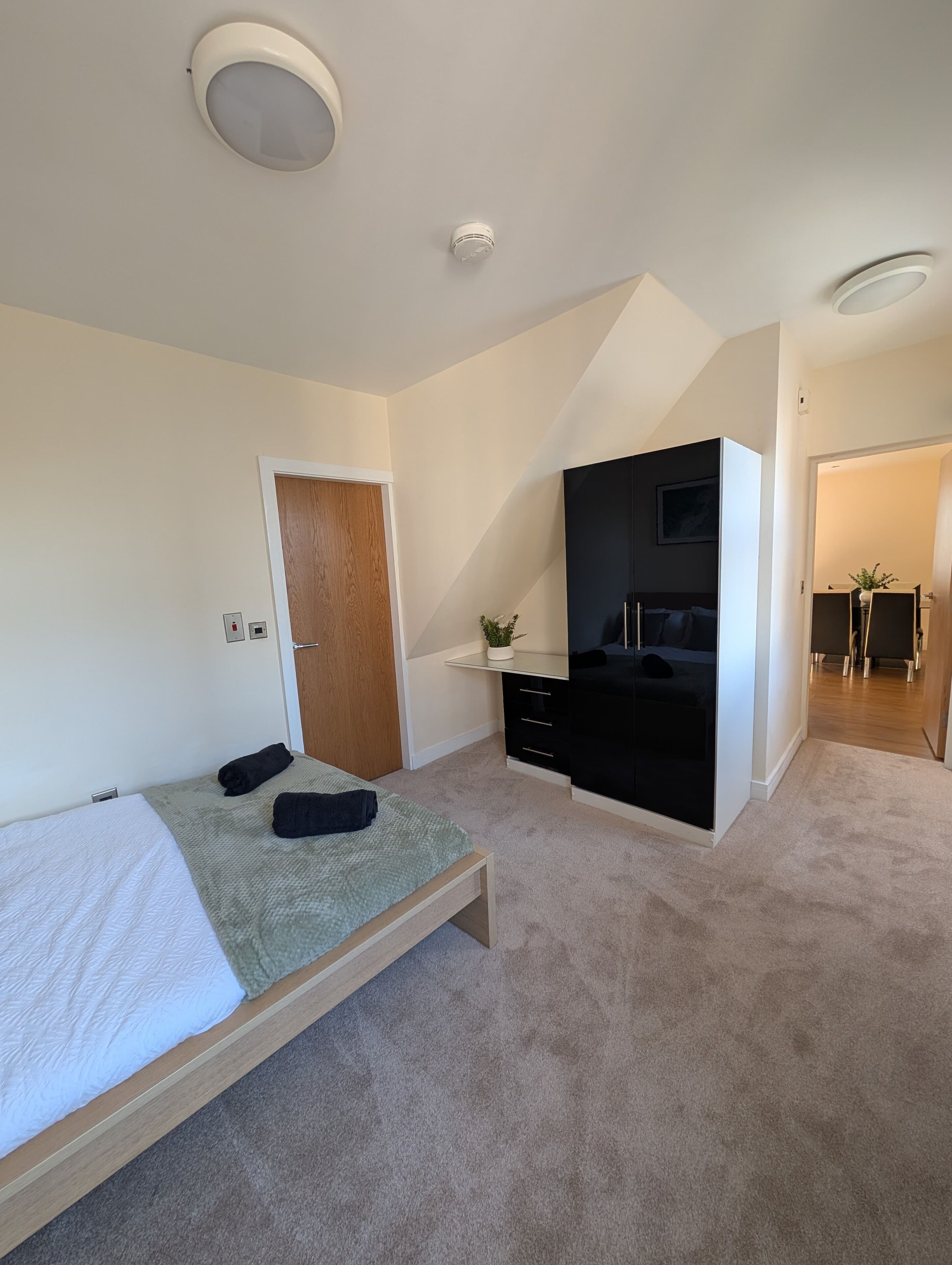 A bedroom with a bed, a desk, a wardrobe, and a door.