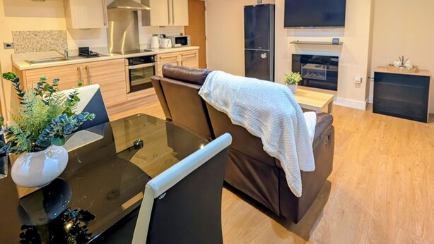 A modern living room with a dining table, sofa, and kitchen area with cabinets and appliances. - Upperhead Row Apartment (Huddersfield)