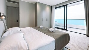 Een moderne hotelkamer met een groot bed, een kledingkast en een balkon met uitzicht op zee.