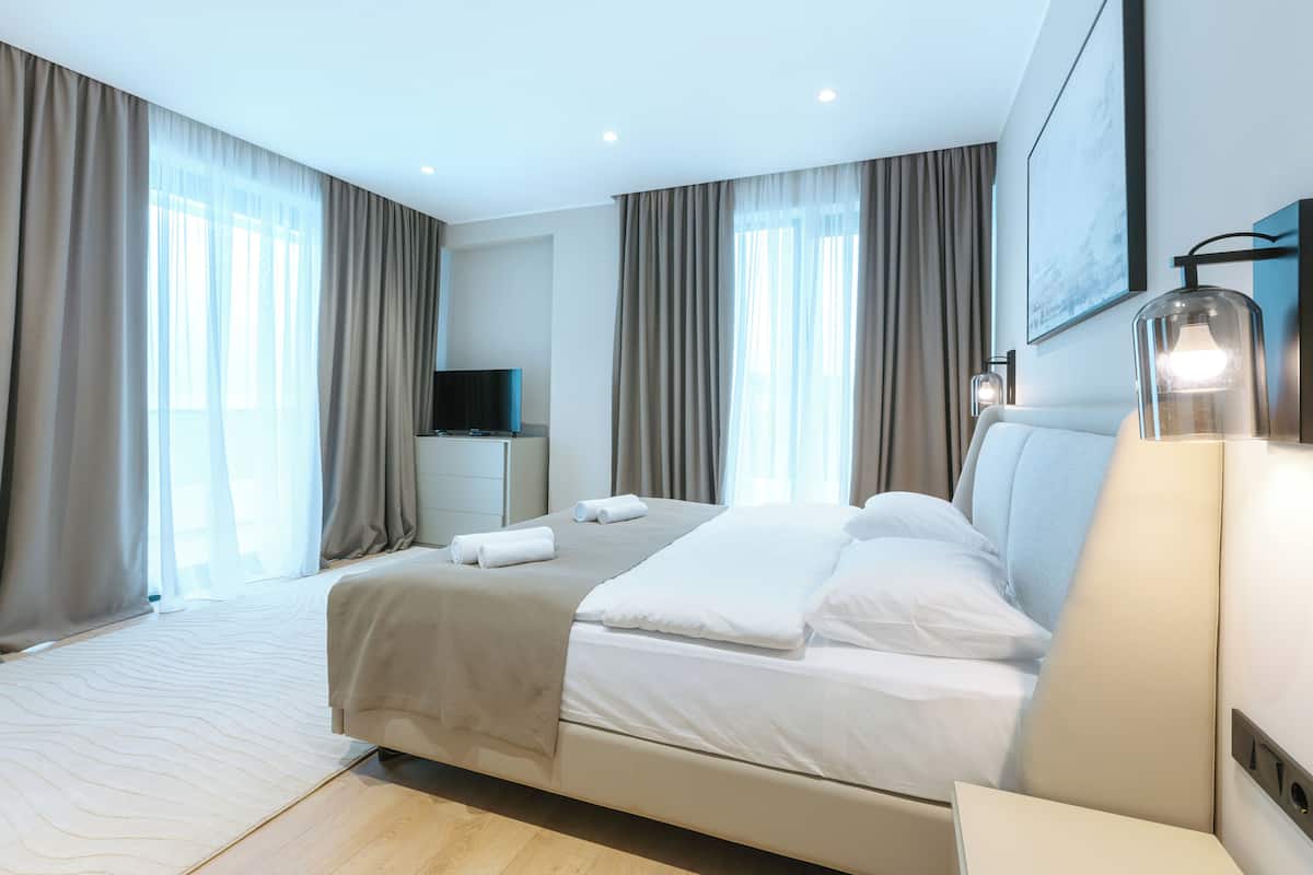Ein modernes Hotelzimmer mit einem großen Bett, einem Flachbildfernseher, einem Nachttisch und einer Lampe.