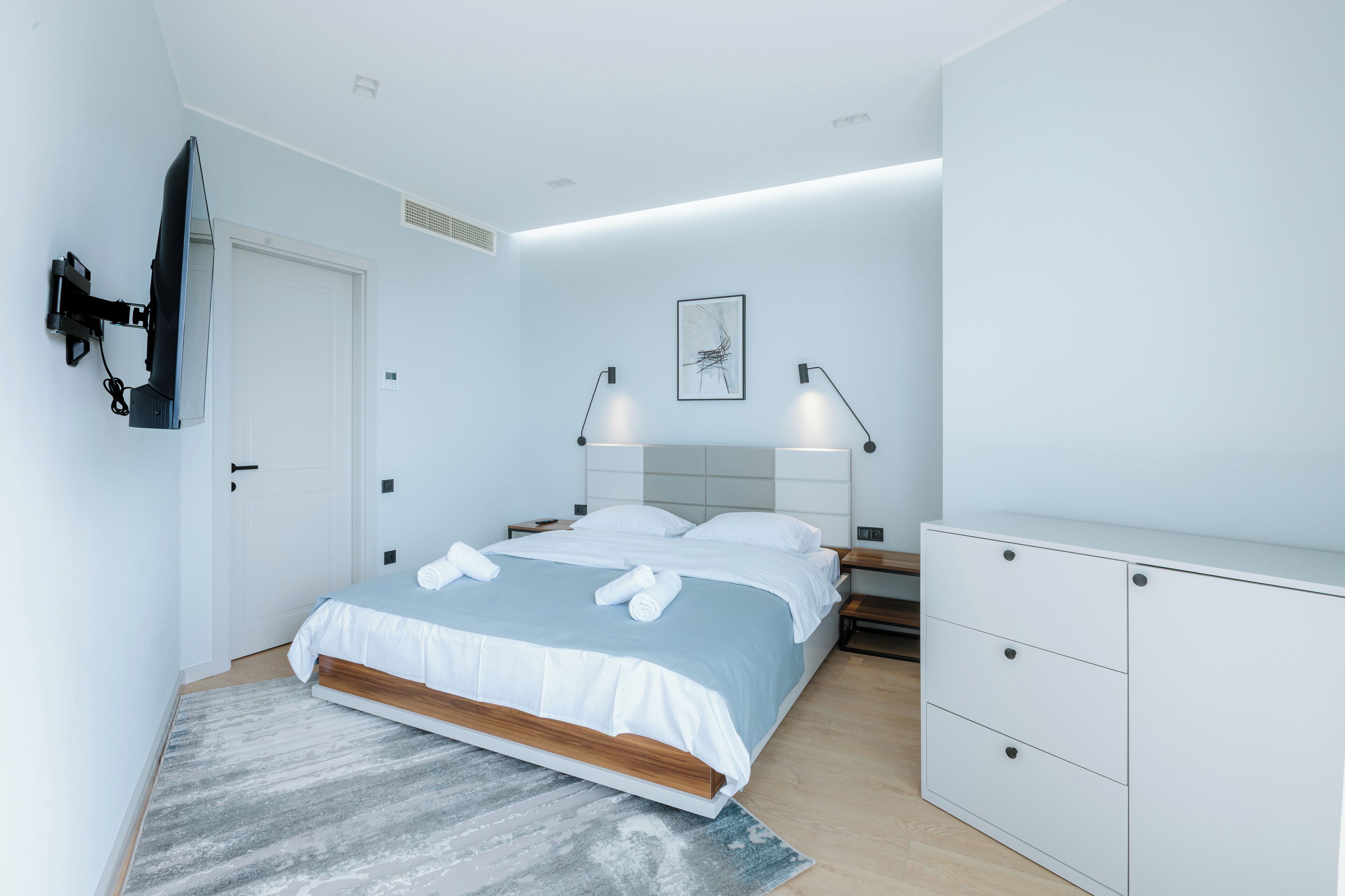 A modern bedroom with a bed, bedside tables, a wardrobe, and a mounted TV.