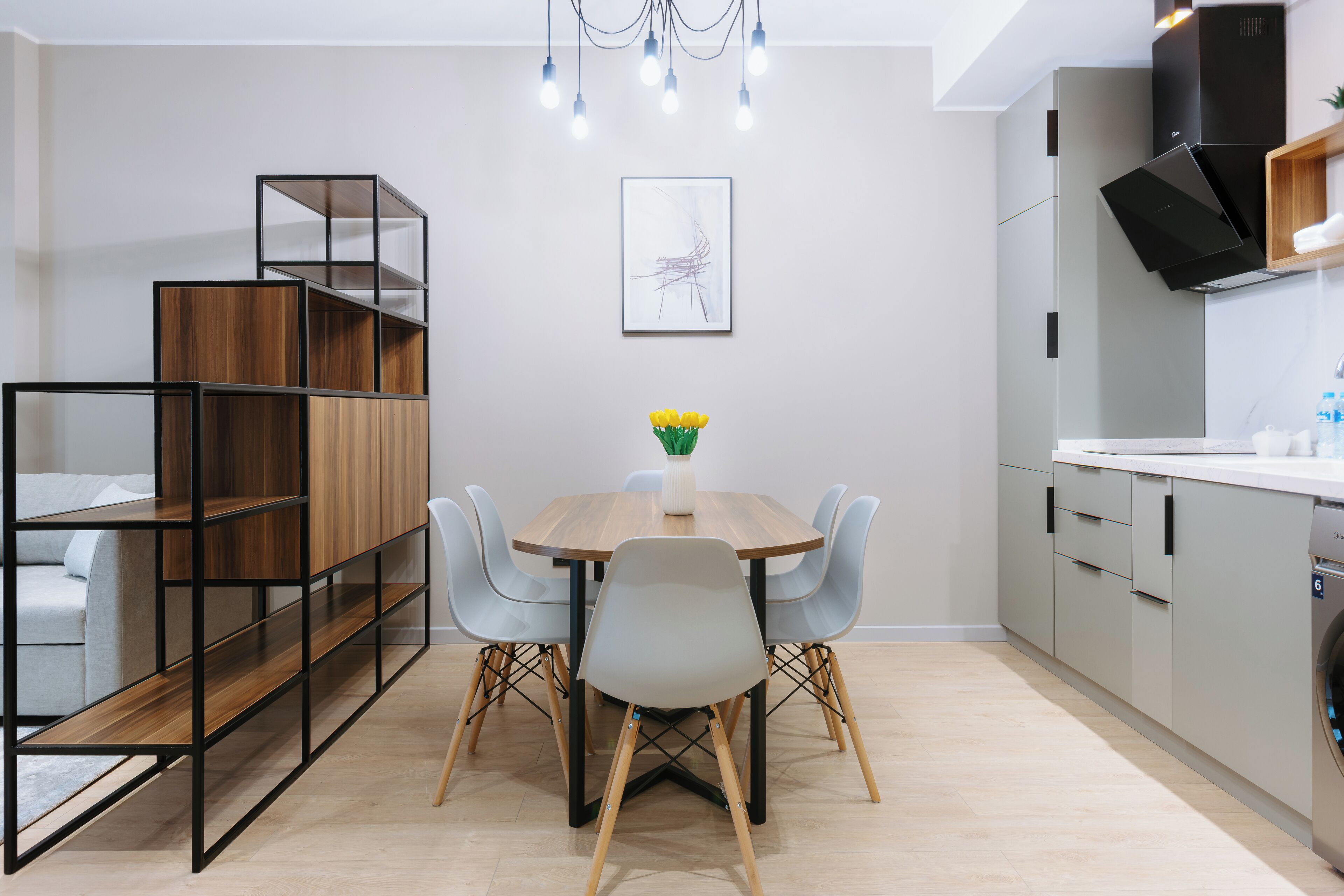 Une cuisine moderne avec un coin repas, comprenant une table en bois, des chaises grises et une bibliothèque intégrée.