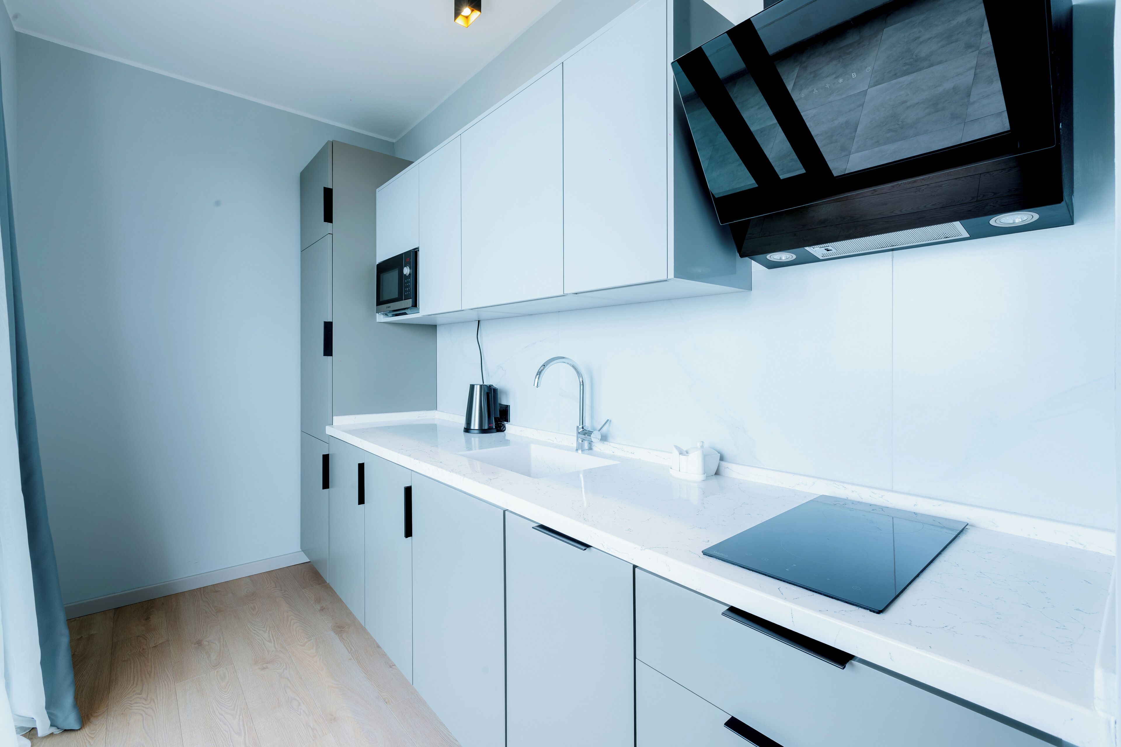 A modern kitchen with white cabinets, a black microwave, and a large black TV mounted on the wall.