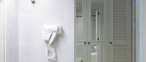 A modern bathroom with a hairdryer mounted on the wall, a glass shower enclosure, and a door with louvered panels.