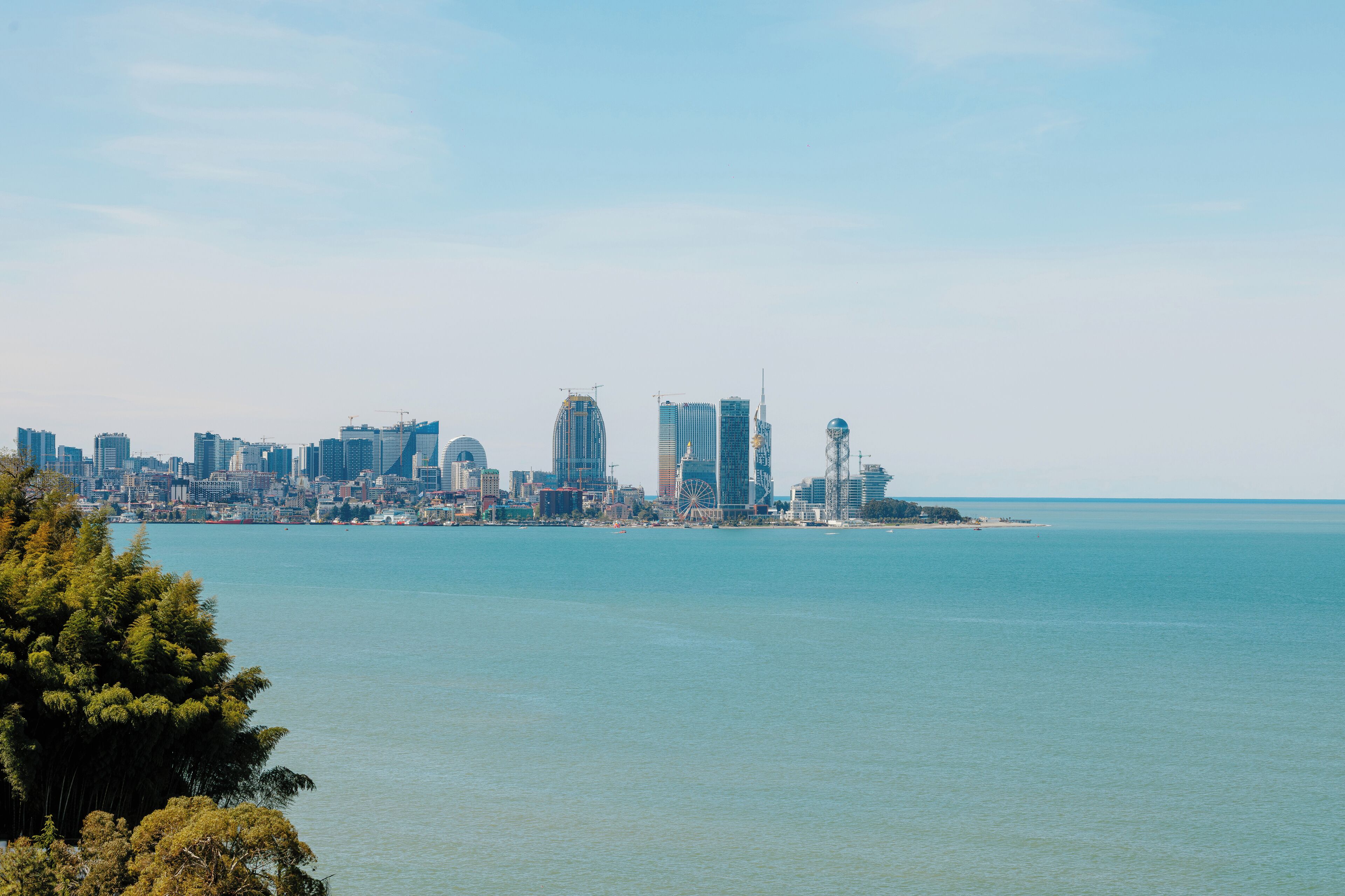 A coastal cityscape with modern high-rise buildings, a clear sky, and a calm sea.
