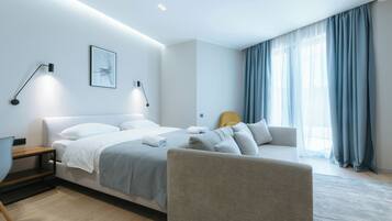 A modern bedroom with a bed, bedside tables, a chair, a sofa, and a large window with curtains.