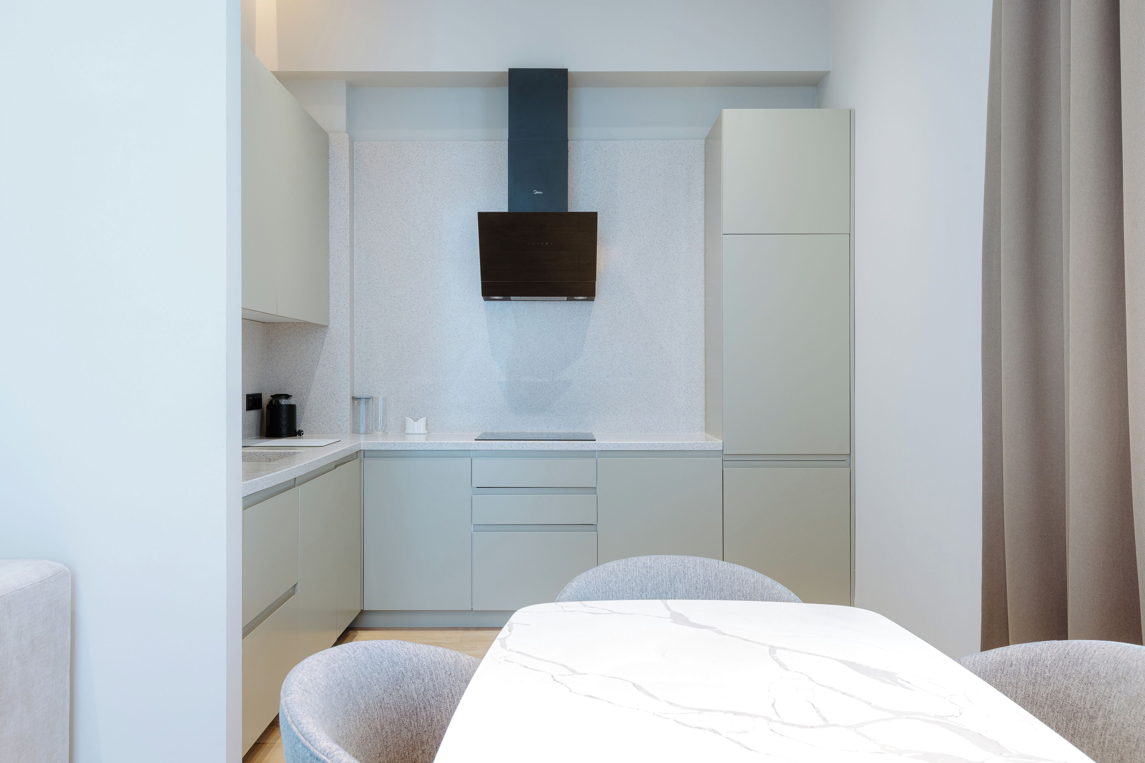 A compact kitchen with a modern design, featuring light-colored cabinetry, a built-in stove, and a flat-screen TV mounted above the stove.