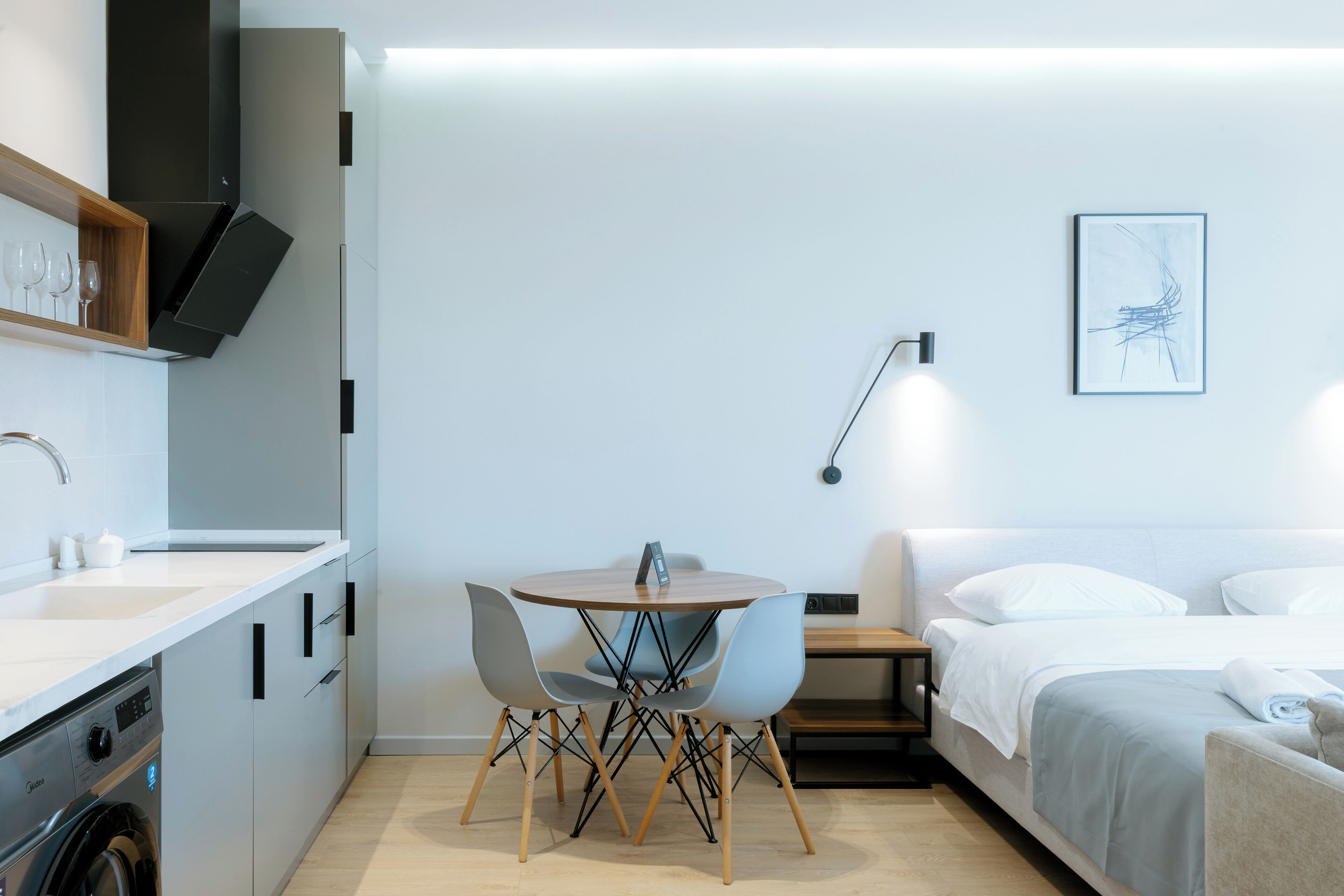 Una habitación de hotel compacta con cama, mesita de noche y una pequeña mesa de comedor con sillas.