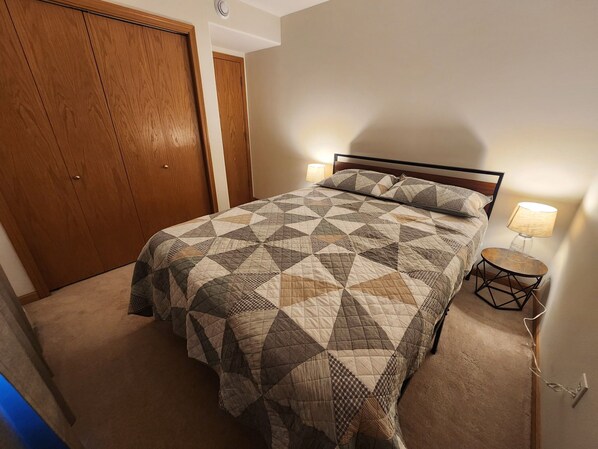 A bedroom with a large bed, a wooden wardrobe, and a bedside table with a lamp.