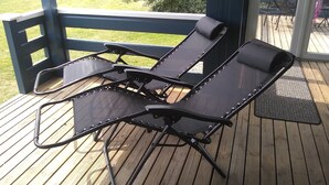 A wooden deck with two black lounge chairs and a metal table.