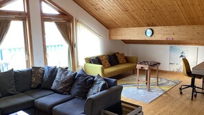 A cozy living room with a grey sofa, a yellow armchair, and a wooden ceiling.