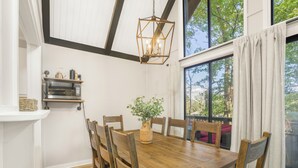 Un comedor con una mesa de madera, sillas, una lámpara colgante y vistas a árboles a través de una ventana.