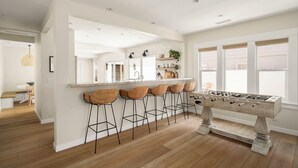 A modern kitchen with a foosball table, bar stools, and a large window. - Belmont Beach Escape: Private Pool and Hot Tub + Steps to the Sand (Long Beach)