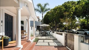 A patio with a table and chairs, a covered seating area, and a gate leading to a street. - Belmont Beach Escape: Private Pool and Hot Tub + Steps to the Sand (Long Beach)