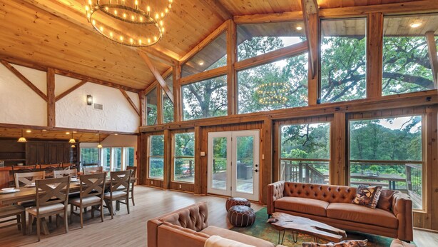 A spacious interior with a large dining area, a cozy seating area, and large windows offering views of the outdoors. - Private Tree Cabin on 8 Acres - King Suite, Large Deck & Fire Pit (Tomball)