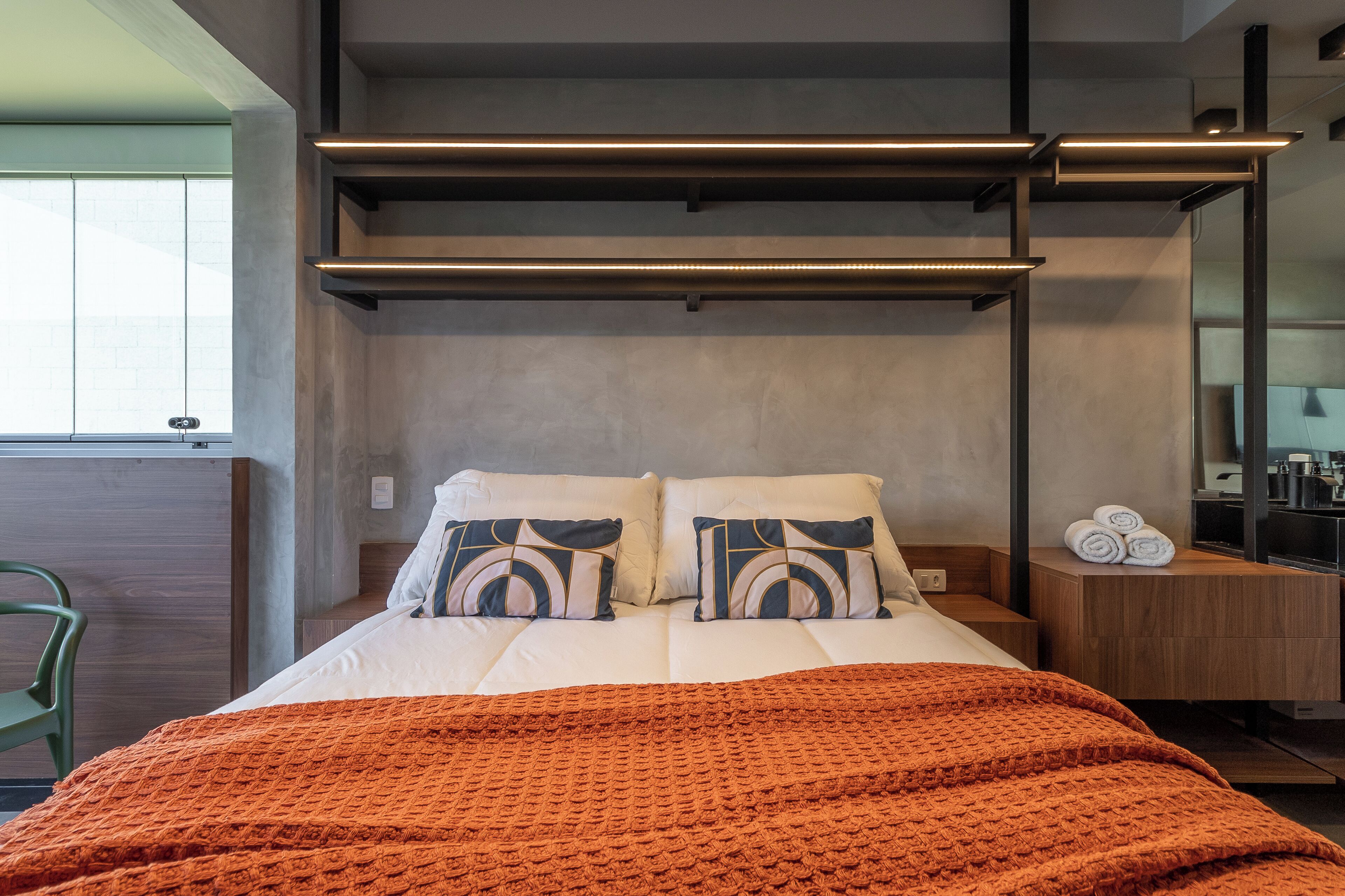 Una habitación de hotel moderna con una cama, dos almohadas, un edredón, una mesita de noche, un espejo y una ventana.
