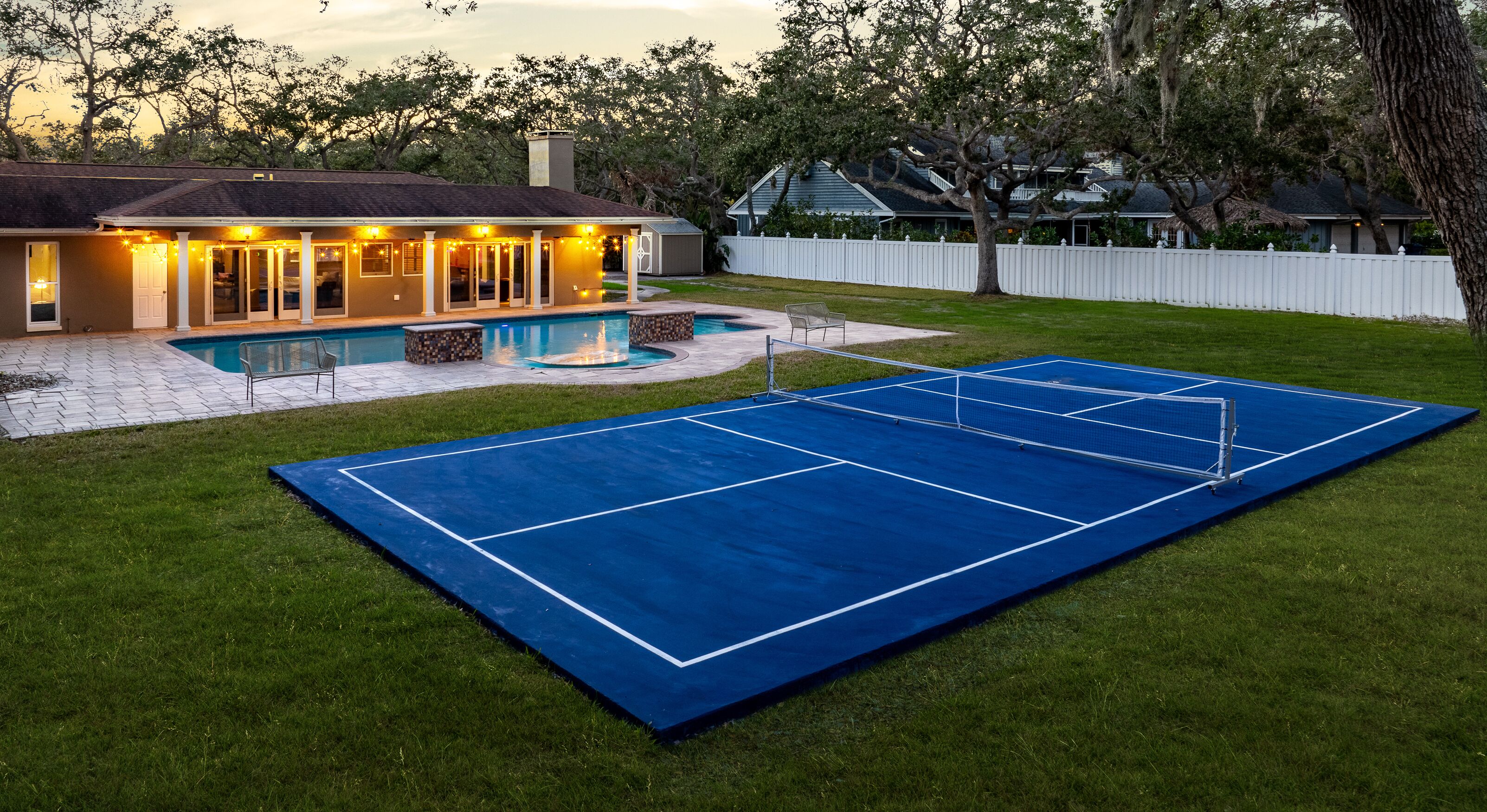 En baghave med tennisbane, swimmingpool og et hus med lyskæder.