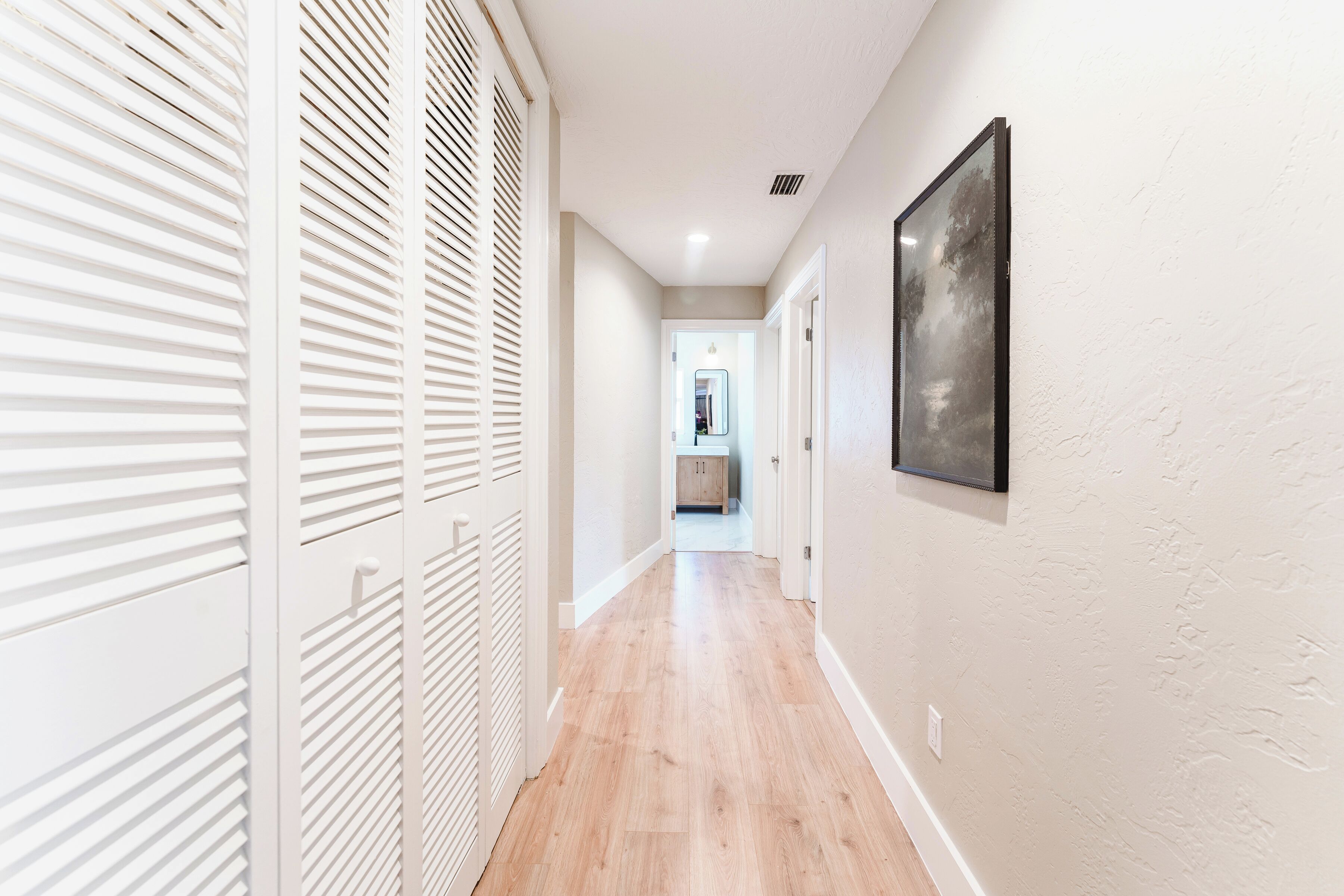 A hallway with wooden flooring, white walls, and a framed picture on the wall.