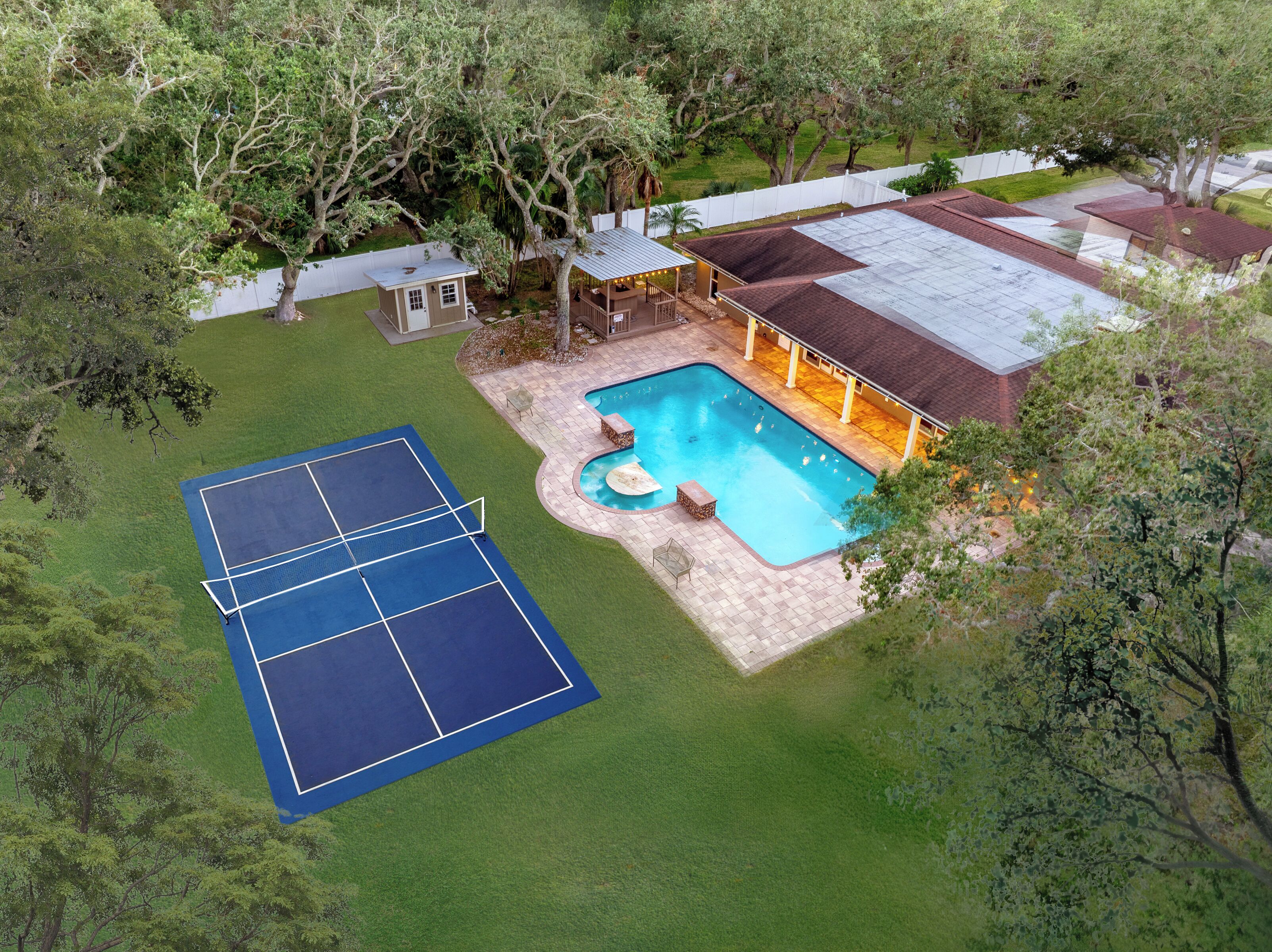 A residential property with a swimming pool, tennis court, and a covered patio area.