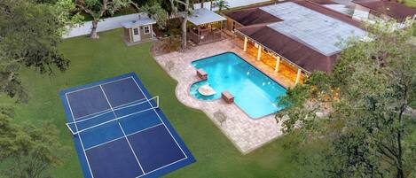 A residential property with a swimming pool, tennis court, and a covered patio area.
