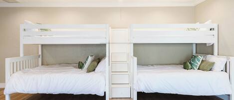 Una habitación con dos literas, suelo de madera y una decoración en tonos blancos.