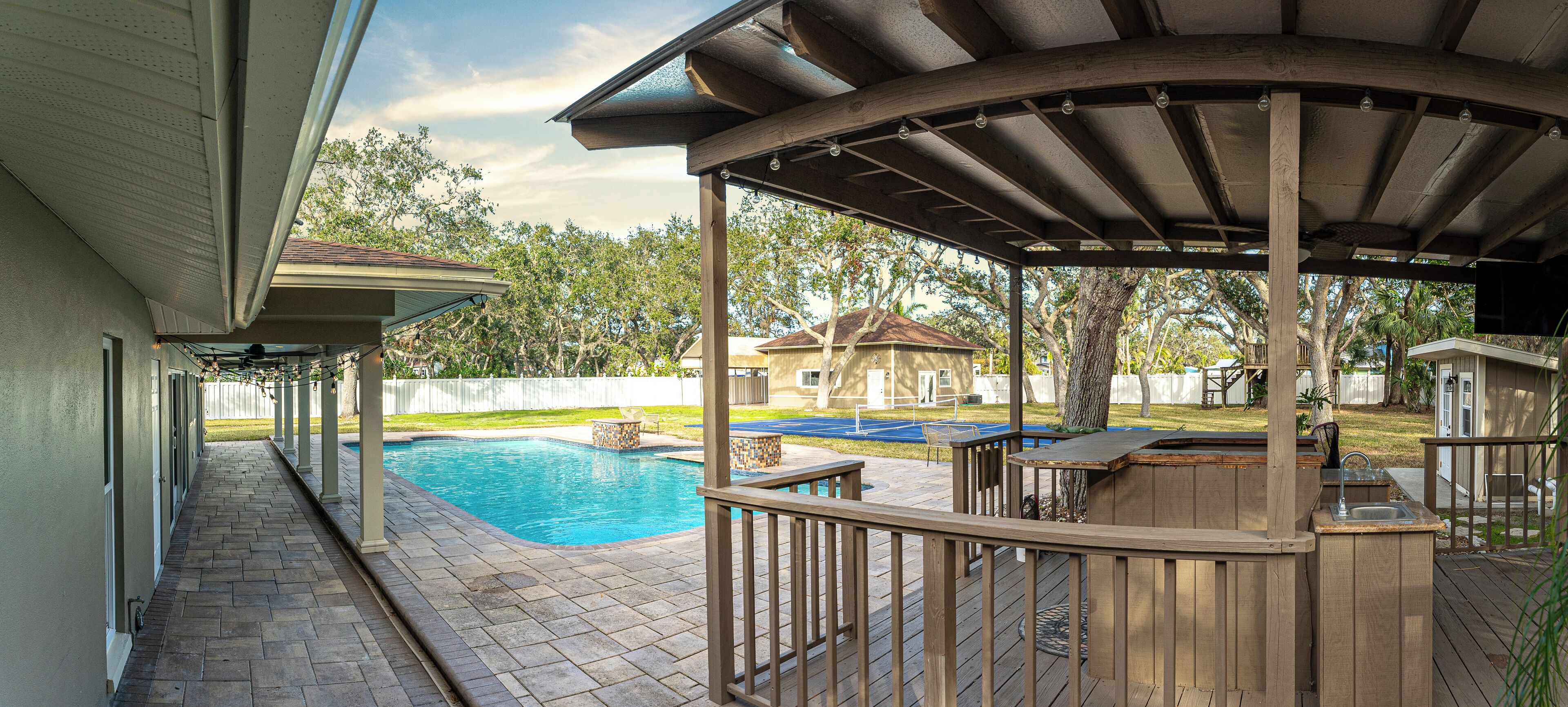 Ein überdachter Außenbereich mit Pool, Holzterrasse und Grillstation.