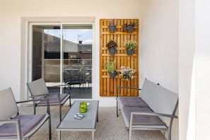 Un patio con due poltrone grigie imbottite, un tavolino con un vaso verde e un muretto in legno con piante in vaso.