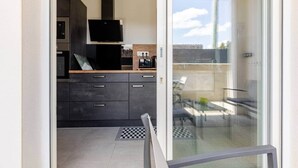 A modern kitchen with dark cabinetry, a flat-screen TV, and a dining area with a glass table and chairs. - "Chez Céline et Frédéric" : house n°1 / T3 60m2 (Rochefort)