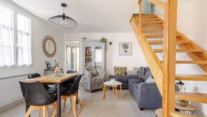 A spacious living area with a wooden staircase, a dining table with chairs, a sofa, and a bookshelf. - "Chez Céline et Frédéric" : house n°1 / T3 60m2 (Rochefort)
