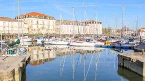 A marina with multiple boats docked, a building with a red roof, and calm water reflecting the boats. - "Chez Céline et Frédéric" : house n°1 / T3 60m2 (Rochefort)