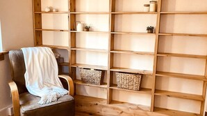A room with a wooden chair covered by a white blanket, a wooden bookshelf with various items, and a woven basket on the floor.