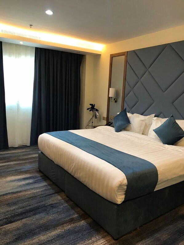 Habitación de hotel con una cama grande, cortinas oscuras, cabecero con diseño de diamantes y suelo alfombrado.