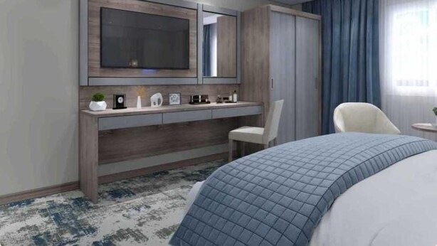 Een moderne hotelkamer met een groot bed, een nachtkastje, een bureau met stoel, een aan de muur bevestigde televisie en een raam met gordijnen.