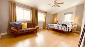 A bedroom with a bed, a sofa, a ceiling fan, and a window. - The Neighbourhood: Expansive loft | free parking (Kingston)
