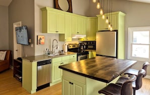 A kitchen with green cabinets, a wooden island, a dishwasher, a stove, and a refrigerator.