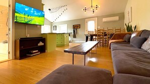 A living room with a sofa, a coffee table, a TV, and a dining area with chairs and a table. - The Neighbourhood: Expansive loft | free parking (Kingston)