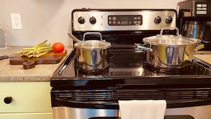 A kitchen with a stove, pots, a cutting board with vegetables, and a coffee maker.